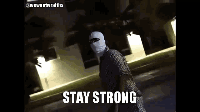 a man wearing a mask and sunglasses is walking down a street with the words stay strong written below him .