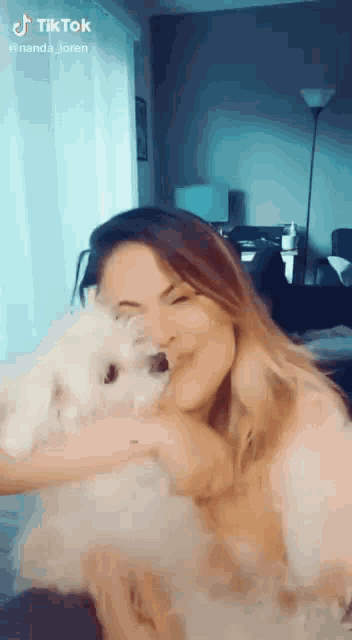 a woman is holding a small white dog in her arms while sitting on a couch .