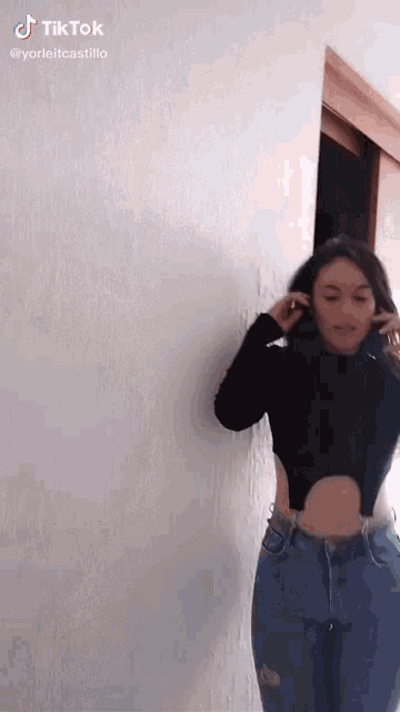 a woman in a black crop top and blue jeans is standing in front of a white wall .