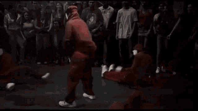 a group of people in red jumpsuits are dancing on a dance floor in front of a crowd .