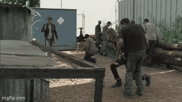 a group of people are standing around a fence and fighting each other .