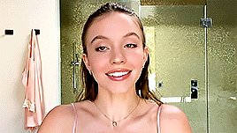 a woman in a pink tank top is smiling in front of a glass shower door .