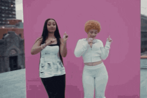 two women are standing next to each other in front of a pink background .