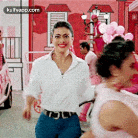 a woman in a white shirt and blue jeans is walking in a room with balloons .