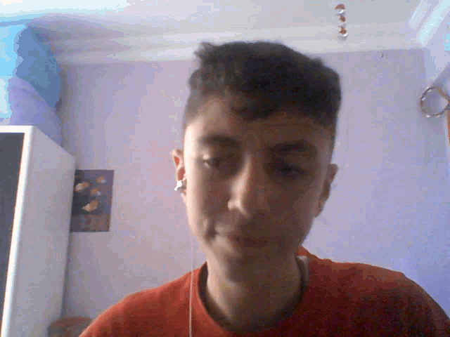 a young man wearing a red shirt and earbuds looks at the camera