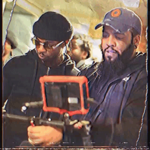a man with a beard is holding a camera and another man is holding a tablet