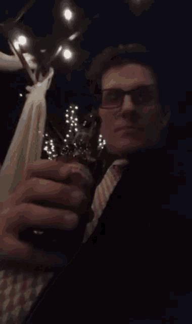 a man with glasses is drinking from a bottle in a dark room