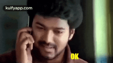 a man is talking on a cell phone with the word ok on his face .