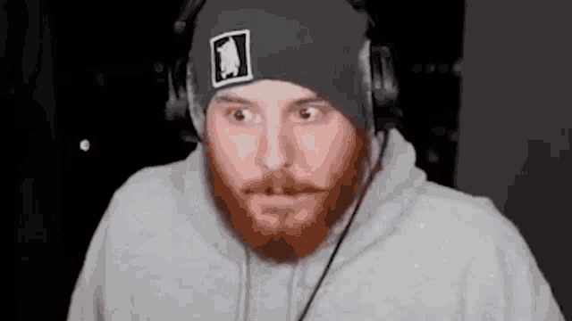 a man with a beard wearing headphones and a beanie is making a funny face .