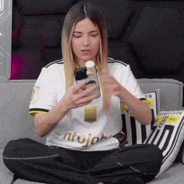 a woman is sitting on a couch looking at her phone and wearing a shirt that says afojob