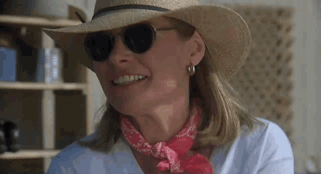 a woman wearing a hat , sunglasses and a bandana is smiling .