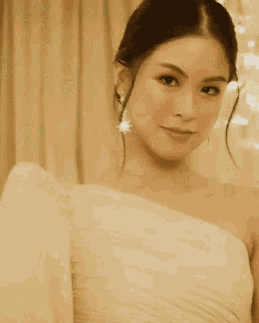 a woman wearing a white dress and earrings is smiling for the camera .