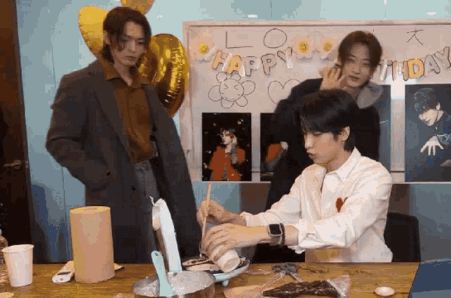 a group of young men are sitting at a table in front of a happy birthday sign