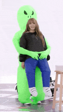 a woman is sitting on the back of an inflatable green alien costume .