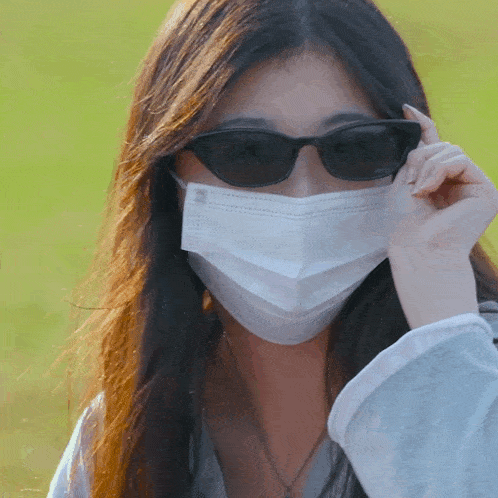 a woman wearing a mask and sunglasses looks at the camera