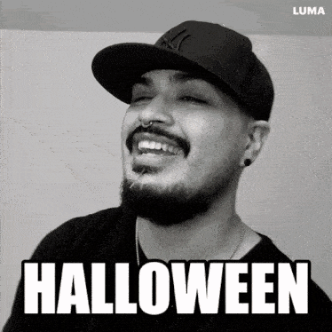a man with a beard wearing a new york yankees hat is smiling and the word halloween is above him