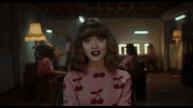a woman in a pink sweater with cherries on it is smiling