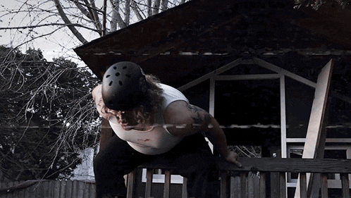 a man wearing a helmet stands on a wooden railing in front of a house