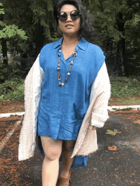 a woman wearing sunglasses and a blue shirt is standing on a road