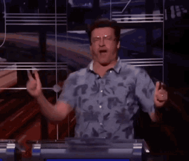 a man wearing glasses and a floral shirt is giving a peace sign