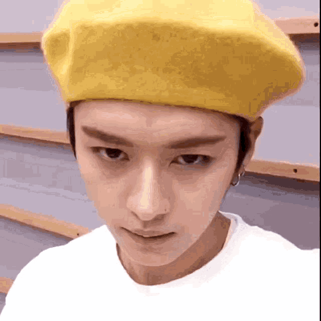 a young man wearing a yellow beret and a white t-shirt .