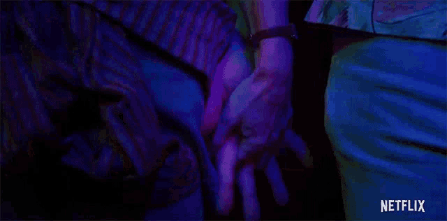 a couple holding hands in a dark room with a netflix logo in the background .