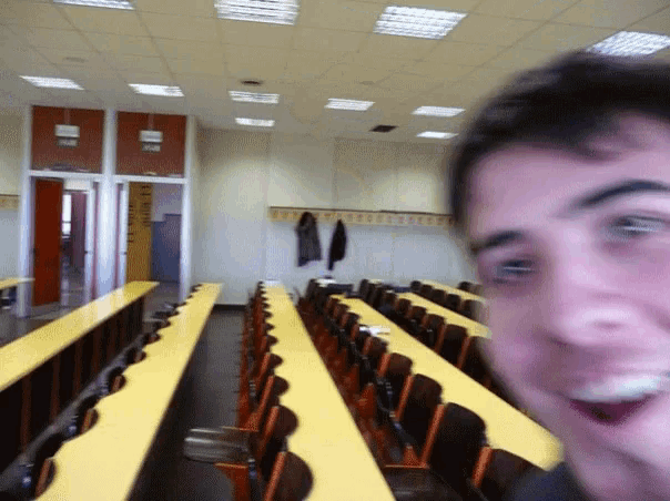 a man taking a picture of himself in a classroom with yellow tables and chairs