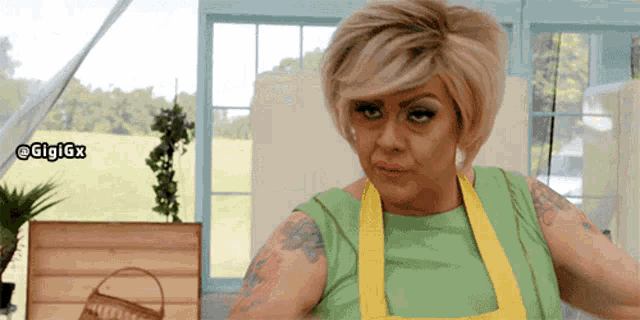 a woman wearing a yellow apron and a green top is looking at the camera