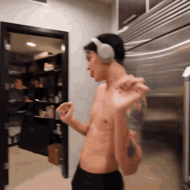 a shirtless man wearing headphones is dancing in a kitchen .