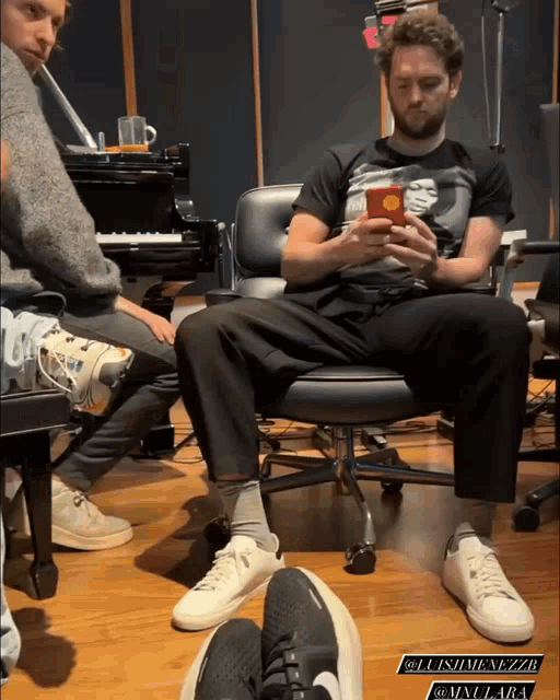 a man sitting in a chair looking at his phone with the name luismenezzb on the bottom right