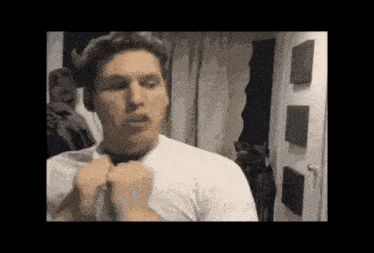 a man in a white shirt is looking at himself in a mirror