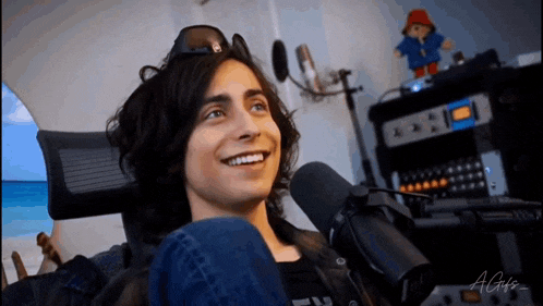 a young man with long hair is sitting in front of a microphone and smiling .