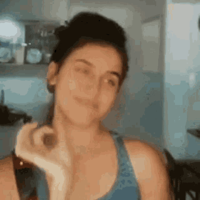 a woman in a blue tank top is making a heart shape with her hands