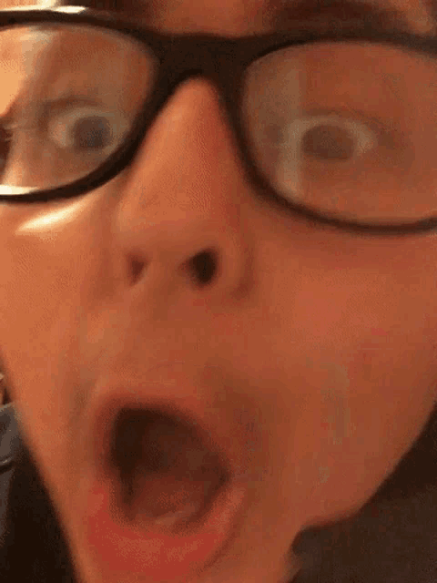 a close up of a person wearing glasses and making a funny face with their mouth open .