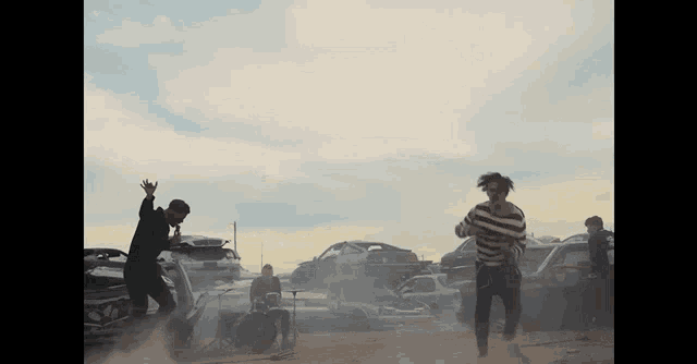 a group of people are dancing in front of a pile of cars