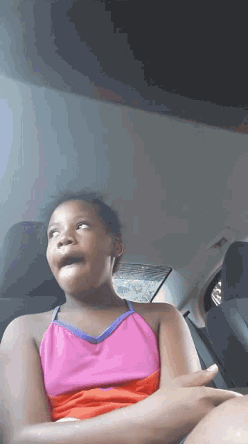 a young girl sitting in the back seat of a car making a surprised face