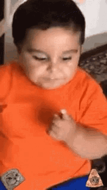 a young boy in an orange shirt is sitting at a table with a slice of pizza .