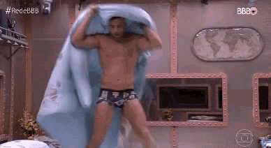 a shirtless man in underwear is holding a blue blanket over his head in a bedroom .