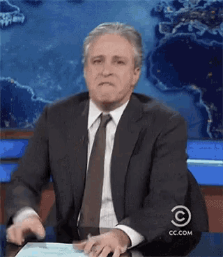 a man in a suit and tie is sitting at a desk with cc.com written on it
