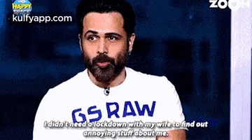 a man with a beard wearing a gs raw shirt is talking on a video call .