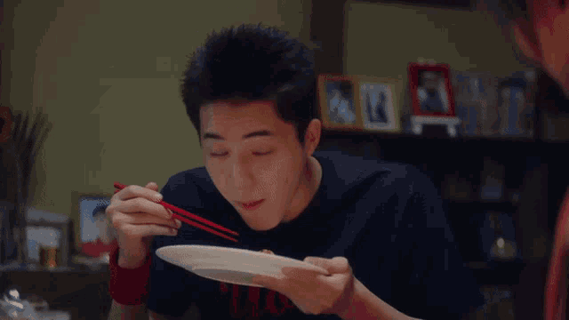 a young man eating with chopsticks and a plate that says ' n.y.c. ' on it