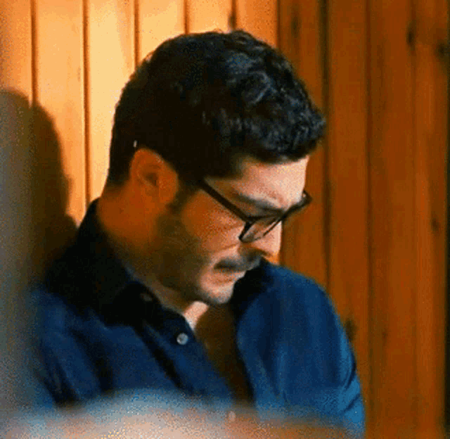 a man wearing glasses is leaning against a wooden wall