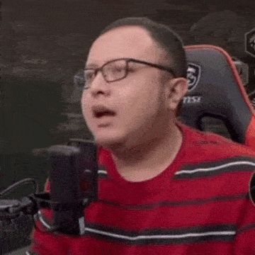 a man wearing glasses and a red shirt is laughing with his mouth open
