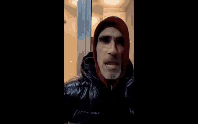 a man with a beard is wearing a hooded jacket and a red hoodie .