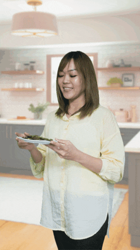 a woman in a yellow shirt is holding a plate of food in a kitchen