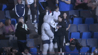 a mascot in a white shirt with a man on it is surrounded by fans