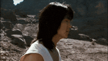 a woman in a white tank top is standing in a desert