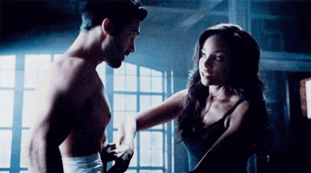 a shirtless man and a woman are standing next to each other in front of a window .