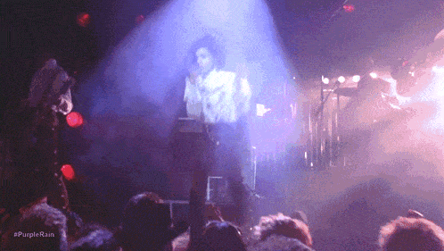 a man singing into a microphone in front of a crowd with the hashtag #purplerain