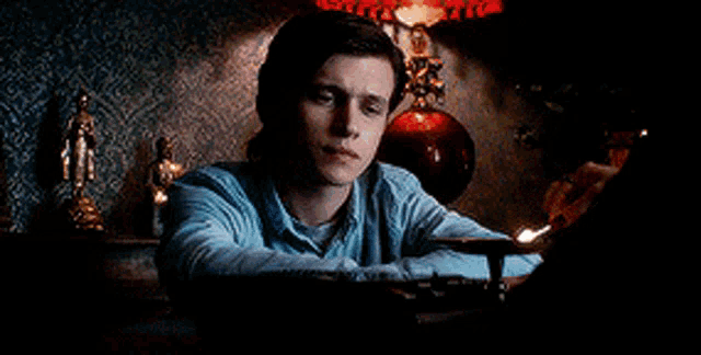 a man in a blue shirt is sitting at a table with a lamp .